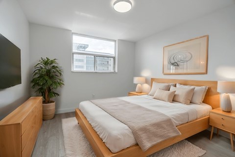 A bedroom with a large bed, a wooden nightstand, and a potted plant. at 70 Park, Mississauga, Canada